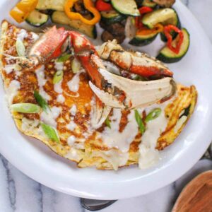 crab omelette with crab legs and veggies on white plate