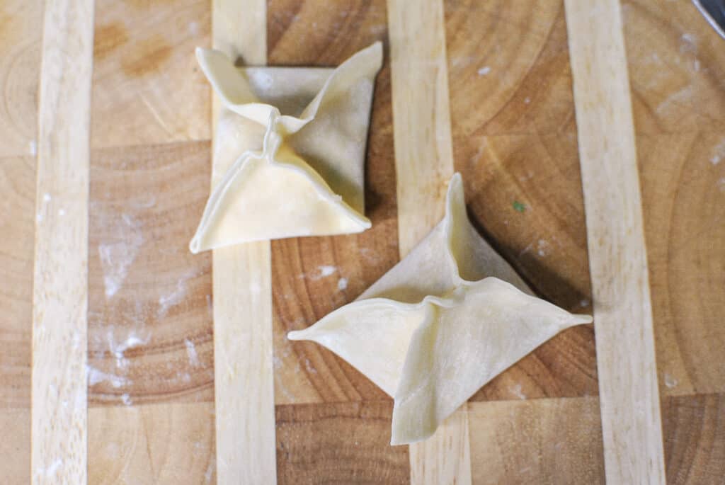 two Crab Rangoon on rustic cutting board