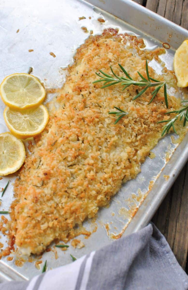 crusted fish with lemons and rosemary on a sheet pan with wood background outdoors
