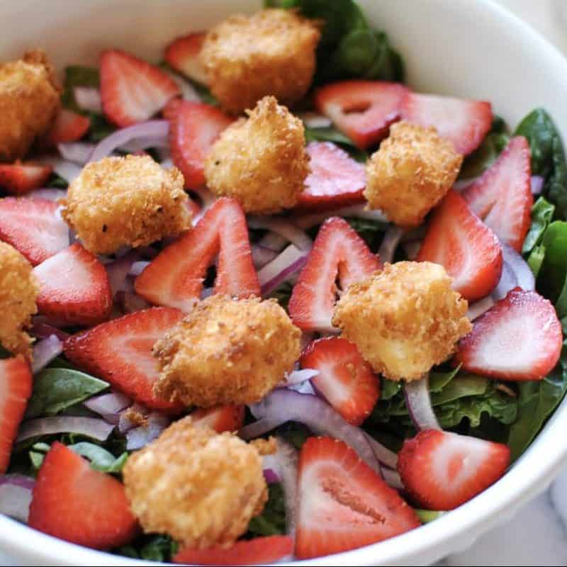 spinach strawberry and fried feta salad recipe in a white bowl with marble background