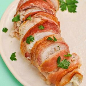 bacon wrapped boursin stuffed fish recipe with parsley garnish on white plate with blue background