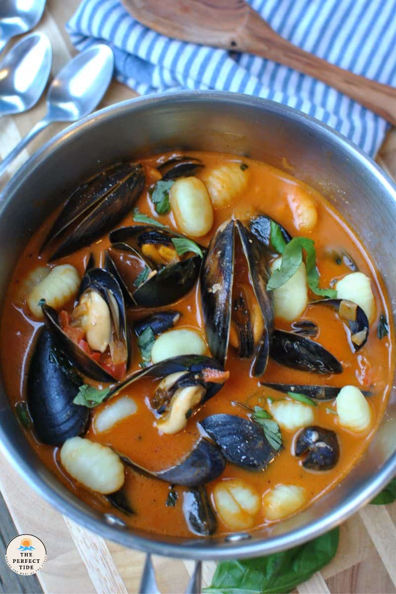 Mussel soup italian style with tomato and red pepper sauce, gnocchi, basil in pot 
