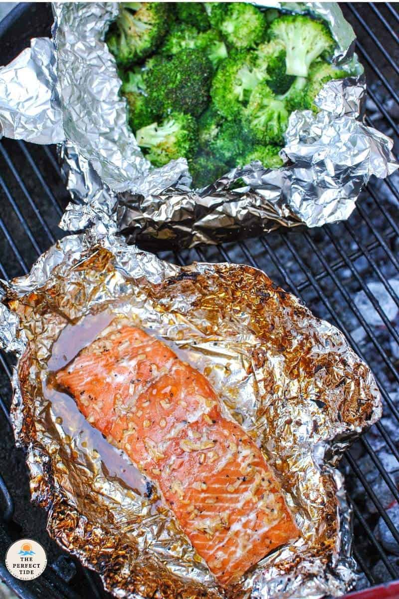 salmon fillet on foil with bourbon brown sugar and chopped onion glaze on bbq grill with broccoli in foil