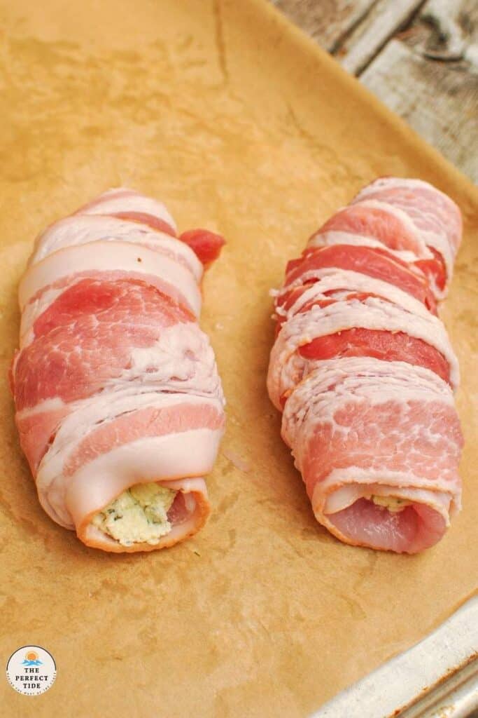 bacon wrapped stuffed white fish with boursin garlic and herb cheese on a parchment paper lined sheet pan