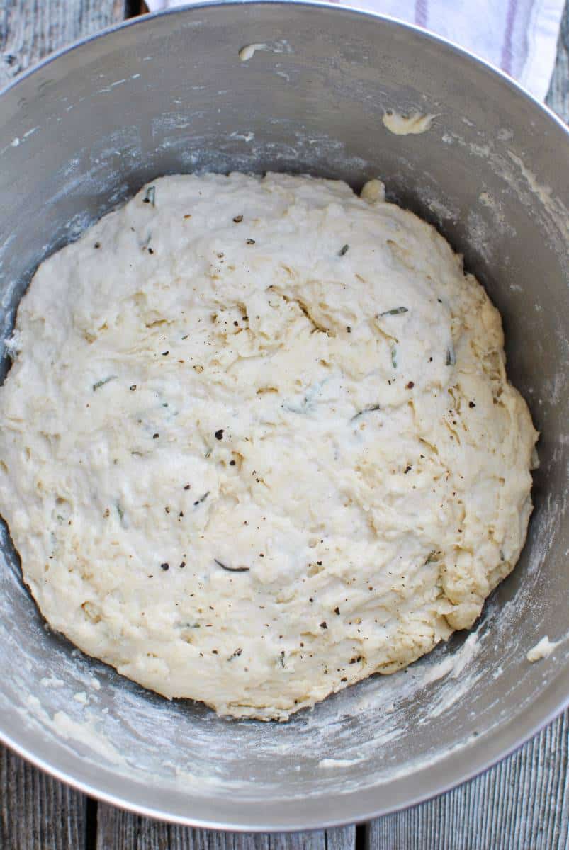 dough with rosemary and parmesan in a metal mixing bowl proofing