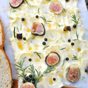 butter board with butter smeared on a marble and wood board with rosemary fresh figs honey and spicy honey along with fresh homemade bread