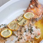 Baked whole rockfish canary rockfish with thyme, lemon slices in white baking dish