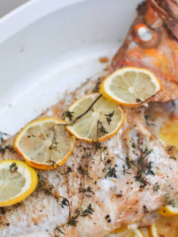 Baked whole rockfish canary rockfish with thyme, lemon slices in white baking dish