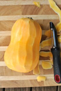 butternut squash peeled on wooden cutting board with peeler