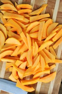 butternut squash cut into strips to make fries on a wooden cutting board