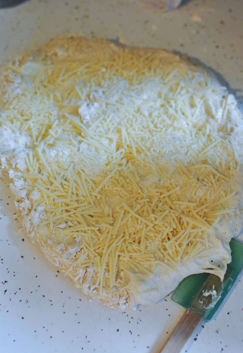 shredded parmesan on dough with blue spatula