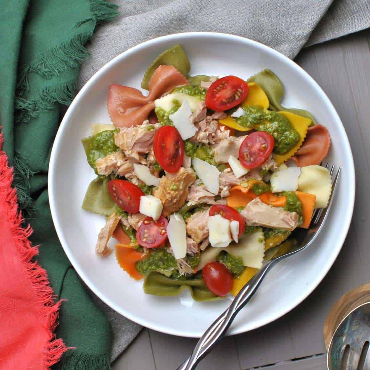 tuna pesto pasta on white plate with fork next to green and pink napkins