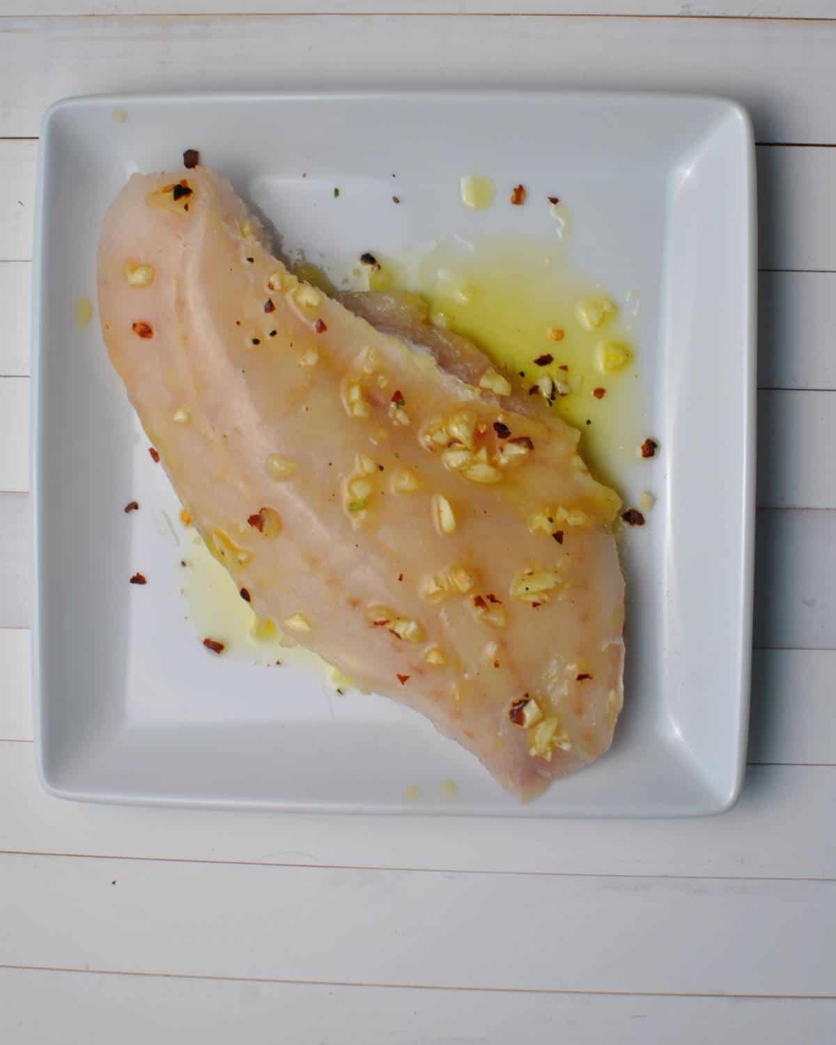 frozen fish fillet on white plate with oil and spices