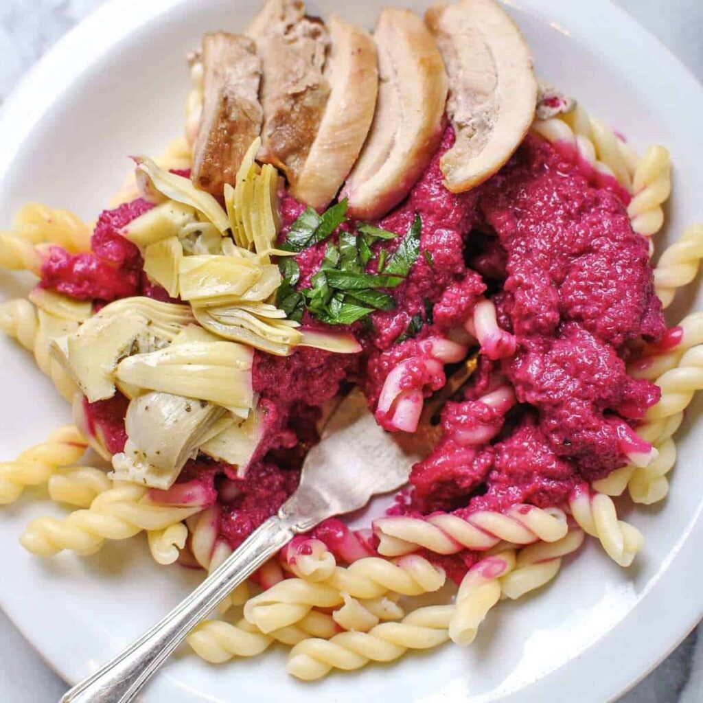 beet sauce pasta plated with artichokes chicken and parsley