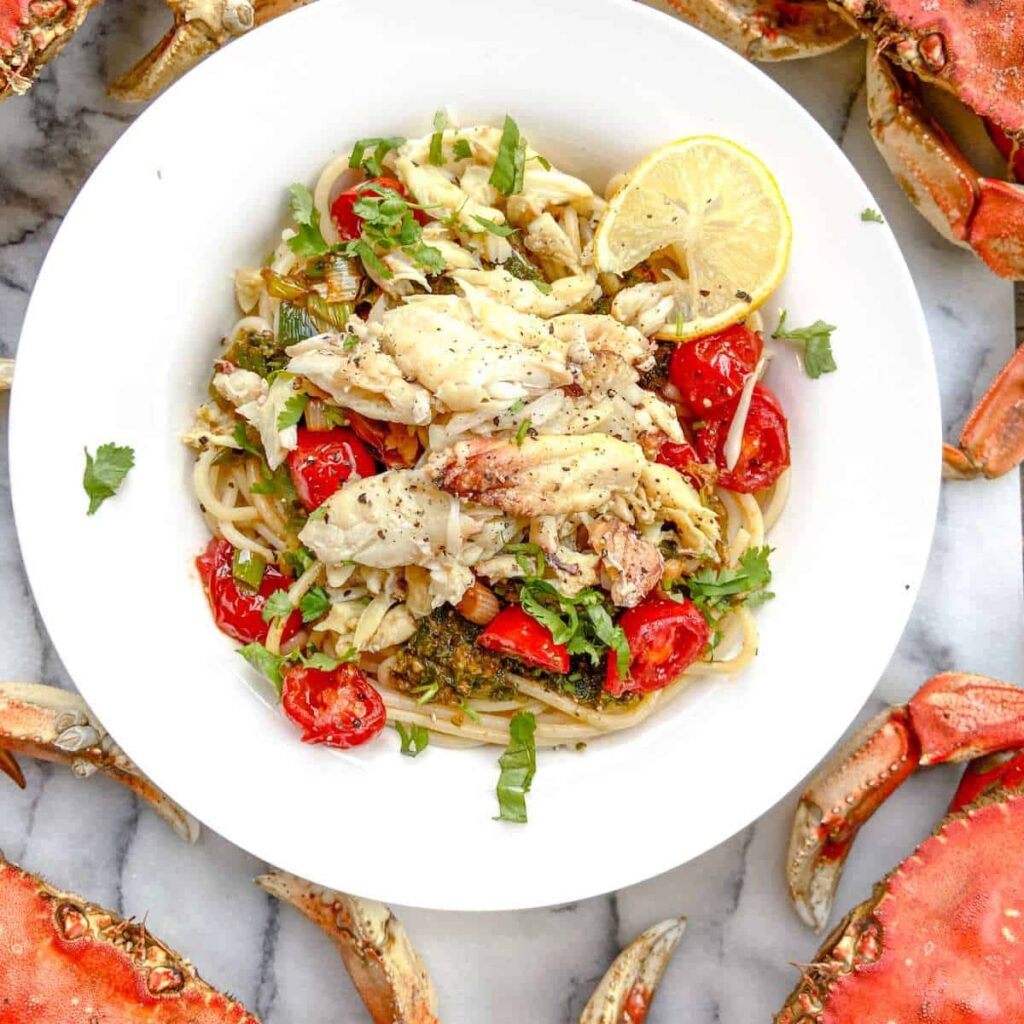 Crab pasta with lemon herb sauce and tomatoes surrounded by dungeness crab
