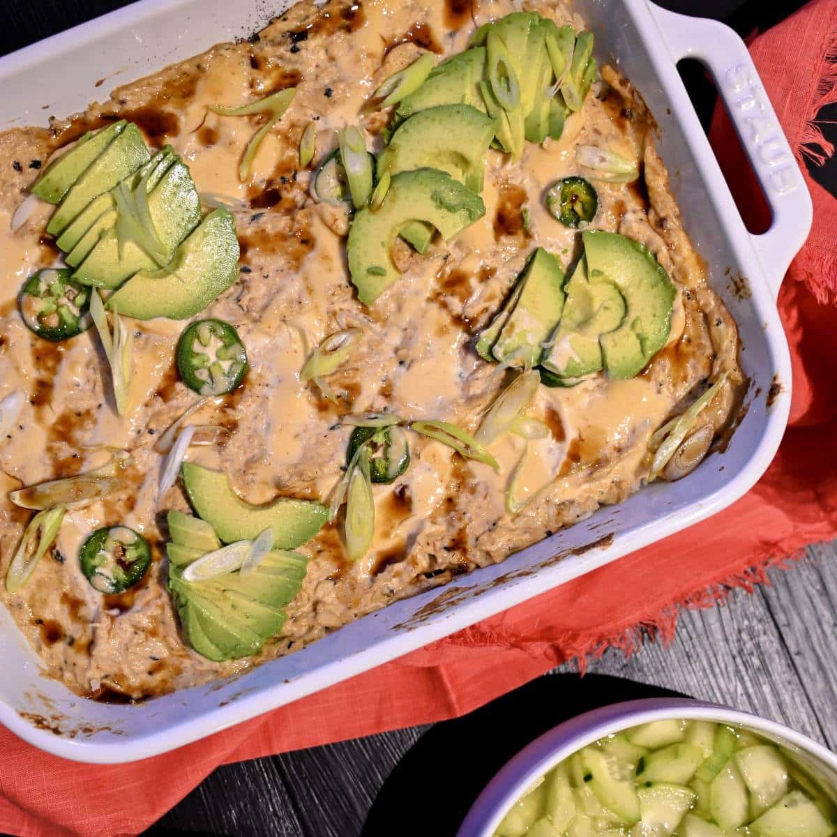 salmon sushi bake in white ceramic casserole dish with avocado and sriracha mayo and jalapenos to top