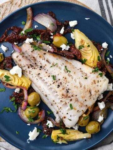Black cod baked with olives artichokes red onion tomatoes feta on blue plate