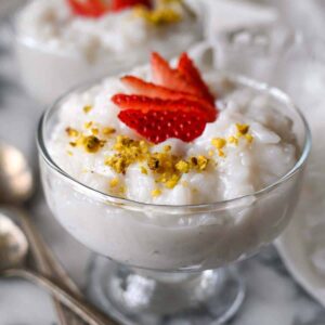 a clear bowl of lebanese rice pudding with strawberry and pistachios as garnish