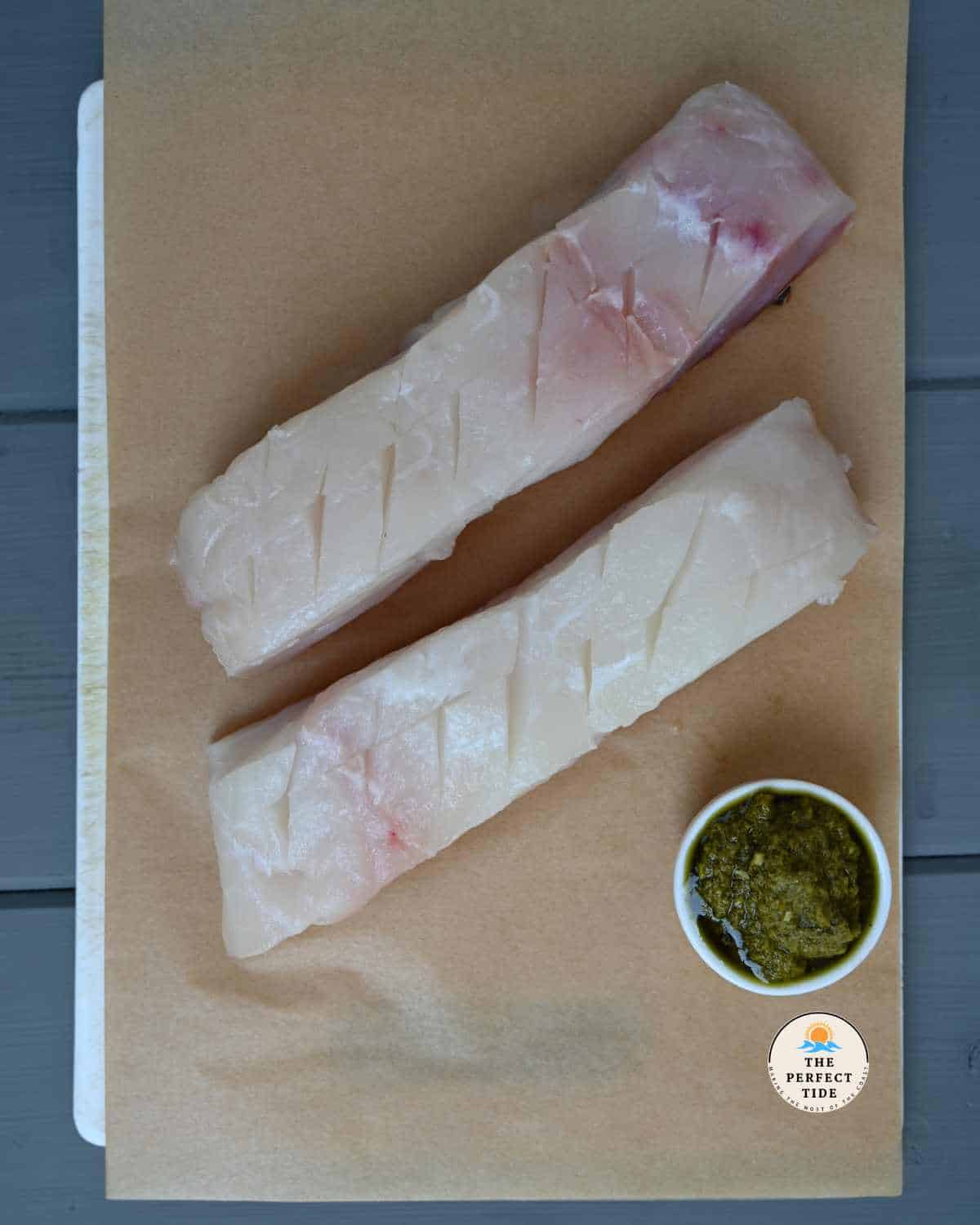 scored halibut with a small jar of pesto on parchment paper