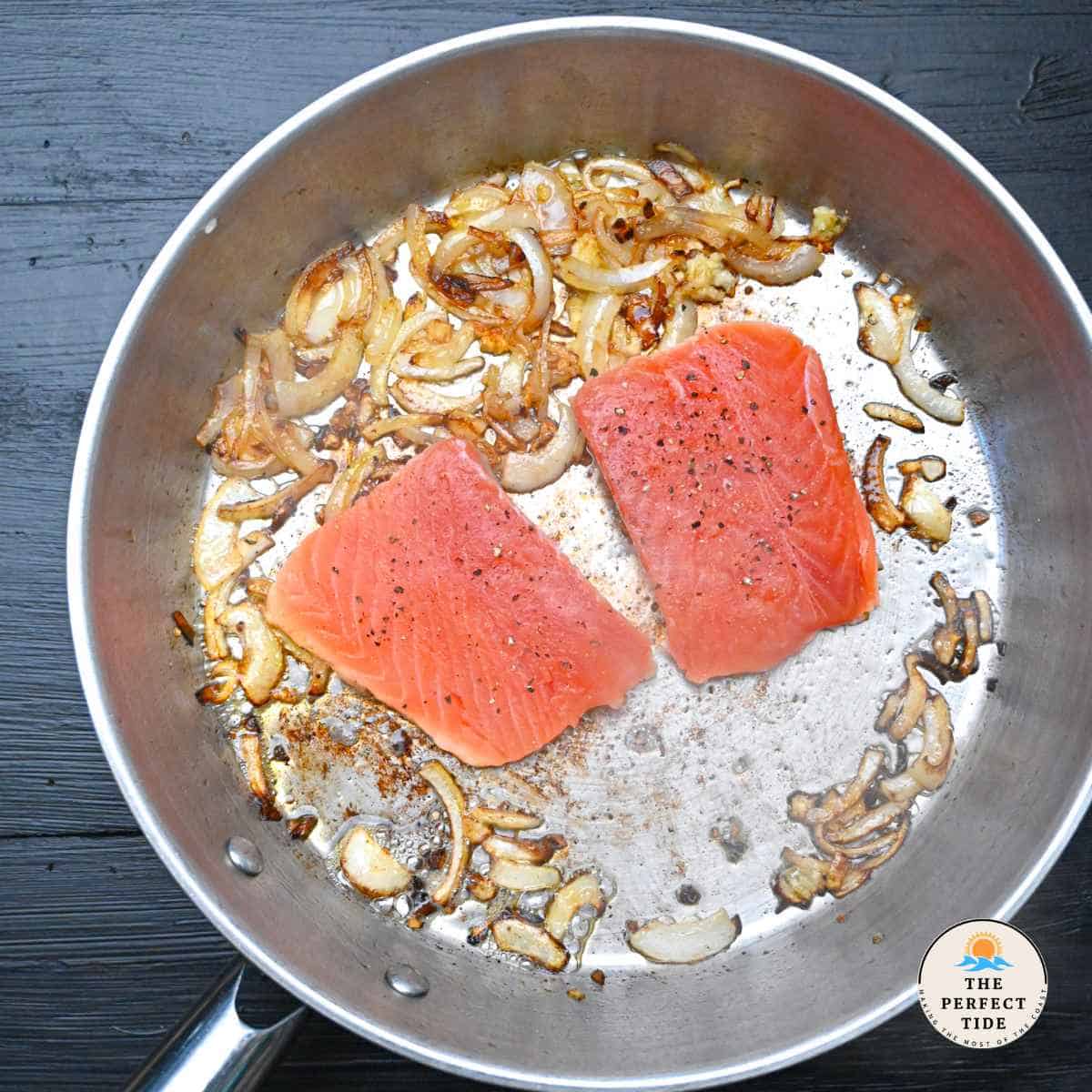 sauteed salmon on skillet with onions garlic and butter