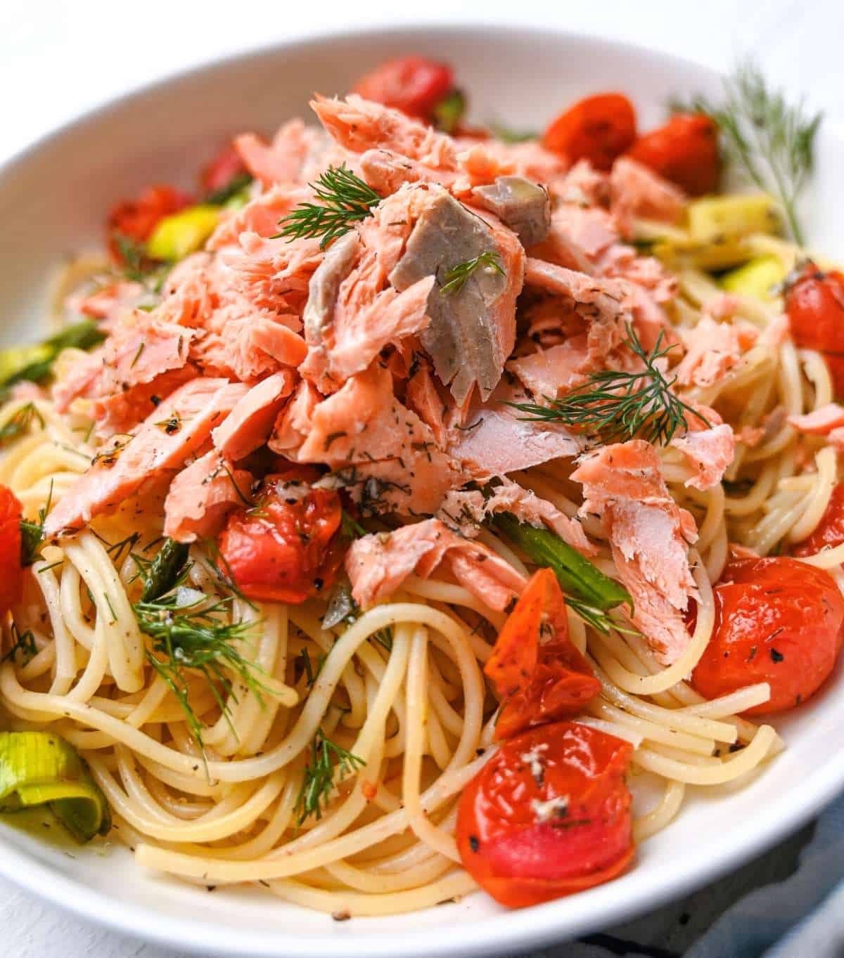 side angle of salmon pasta without cream in white dish with roasted cherry tomatoes leeks asparagus