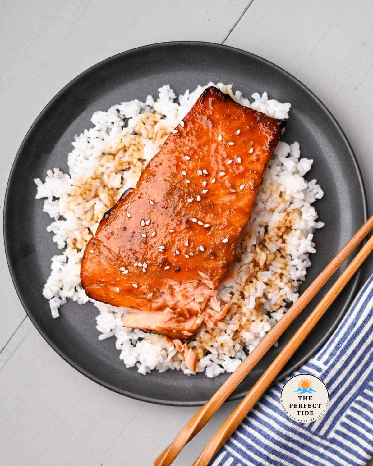 air fryer teriyaki salmon with sesame seeds on a bed of rice and chopsticks
