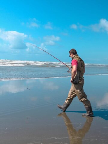 a man surf fishing for perch in waders