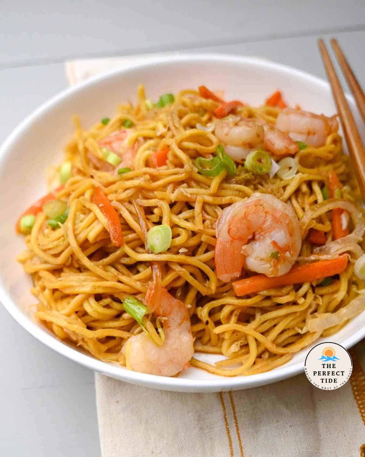 shrimp yakisoba with carrots noodles onion in a white bowl with chopsticks