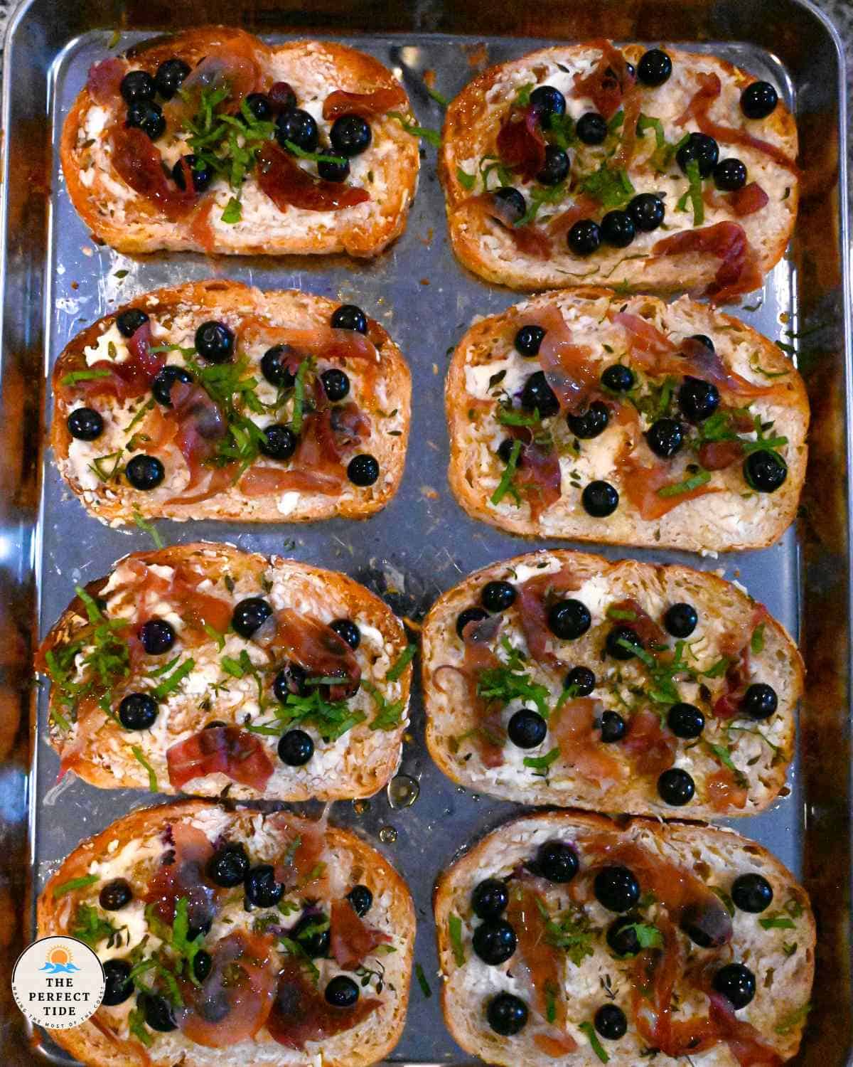 sourdough bread toasted with goat cheese and blueberries topped with prosciutto and herbs 