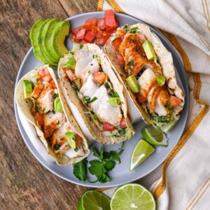 fish tacos with slaw and crema on plate with avocado lime and cilantro