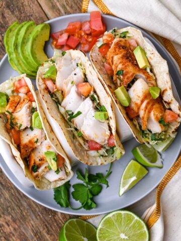 fish tacos with slaw and crema on plate with avocado lime and cilantro