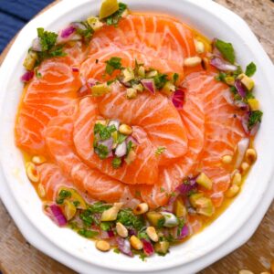 salmon crudo with a herb citrus dressing and pine nuts on a white place