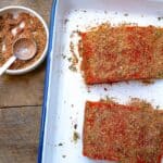 salmon rub in a bowl near a sheet pan of salmon that have dry rub on them