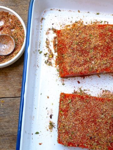 salmon rub in a bowl near a sheet pan of salmon that have dry rub on them