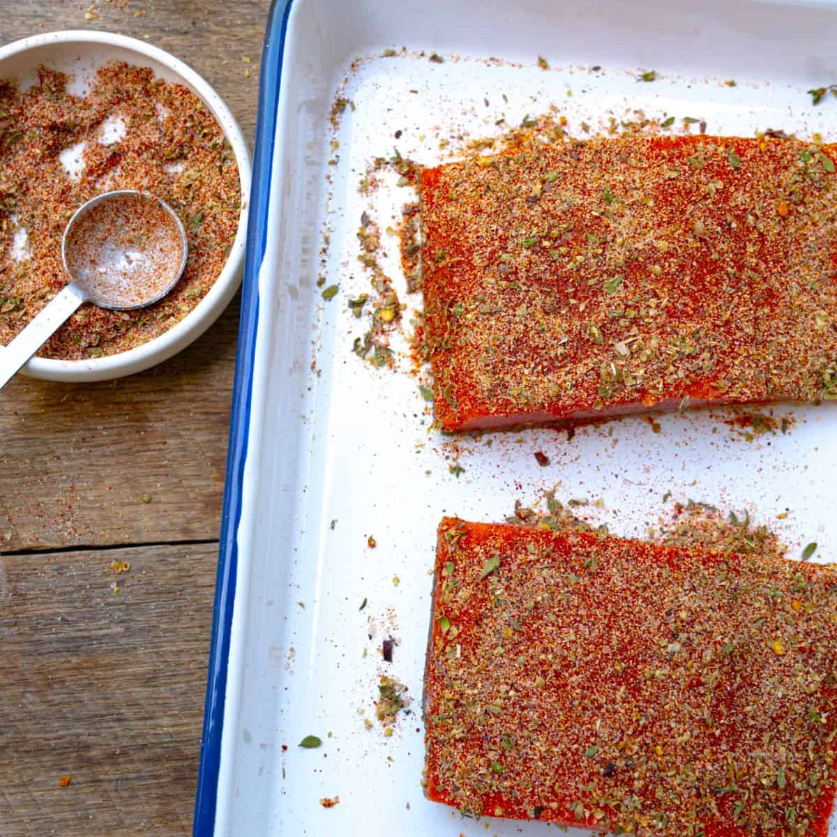salmon rub recipe in a bowl near a sheet pan of salmon that have dry rub on them