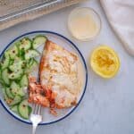 air fryer frozen salmon recipe in plate next to air fryer basket with cucumber salad