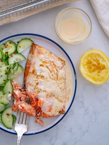 air fryer frozen salmon recipe in plate next to air fryer basket with cucumber salad